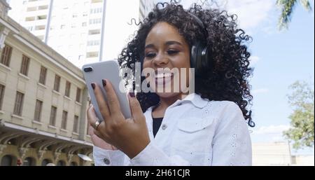Junge lockige schwarze Frau, die mit dem Handy läuft. SMS auf der Straße. Große Stadt. Stockfoto