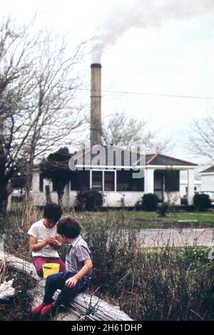 Kaiser Aluminium-Anlage rauchestack verraucht über dem Wohngebiet des Chalmette-Abschnitts von New Orleans, Kinder spielen im Vordergrund ca. März 1973 Stockfoto