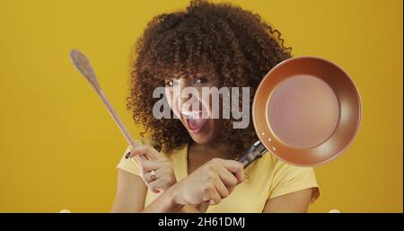 Kochutensilien. Kochfrau in der Küche mit Bratpfanne und Holzlöffel. Hausfrau tanzt. Stockfoto