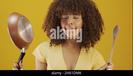 Kochutensilien. Kochfrau in der Küche mit Bratpfanne und Holzlöffel. Hausfrau tanzt. Stockfoto