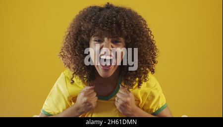 Unterstützer Brasiliens. Brasilianisches lockiges Haar Frau Fan feiert auf Fußball, Fußballspiel auf gelbem Hintergrund. Brasilianische Farben. Stockfoto