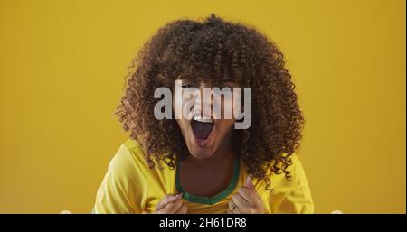 Unterstützer Brasiliens. Brasilianisches lockiges Haar Frau Fan feiert auf Fußball, Fußballspiel auf gelbem Hintergrund. Brasilianische Farben. Stockfoto