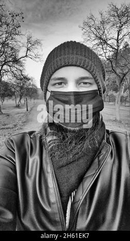 Vertikale Graustufenaufnahme einer südasiatischen Person in einer OP-Maske und einer Wintermütze an einem kalten Tag Stockfoto