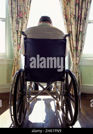 Mann im Rollstuhl mit Blick aus dem Fenster. Häusliche Gesundheitsfürsorge für Kranke, Behinderte und Kranke. Einsamkeit im Alter für Behinderte. Gesundheitswesen Gesundheit Angst. Stockfoto