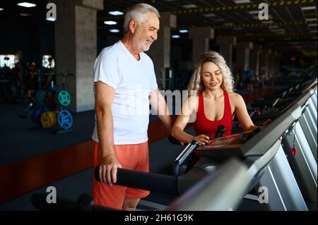 Alter Mann auf dem Laufband, weibliche Personal Trainer Stockfoto