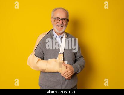 Reifer Mann mit einer Armschiene lächelt auf Kameraszeichen isoliert auf gelbem Hintergrund Stockfoto