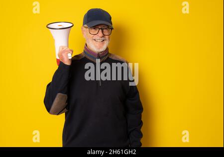 Reifer Mann trägt Kappe hält Megaphon isoliert über gelbem Hintergrund. Stockfoto