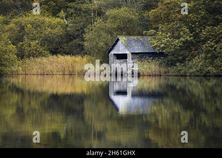 Blick über die ruhige aussicht auf das alte Bootshaus, das sich am Ufer des Rydal Water im Lake District befindet, Herbst gleich um die Ecke. Stockfoto