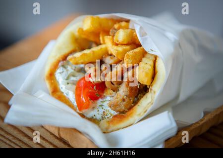 Souvlaki-Sandwich mit Tzatziki-Sauce, gebratenem Küchenfleisch, Pommes frites und frischem Gemüse in Pitabrot verpackt. Traditionelles griechisches Fast-Food-Gericht Stockfoto
