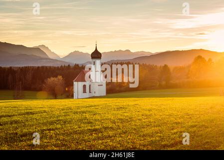 Die Barockkapelle St. Johann über dem Loisachtal und die herbstlichen bayerischen Alpen mit Zugspitze im Hintergrund der Abendsonne, Deutschland Stockfoto