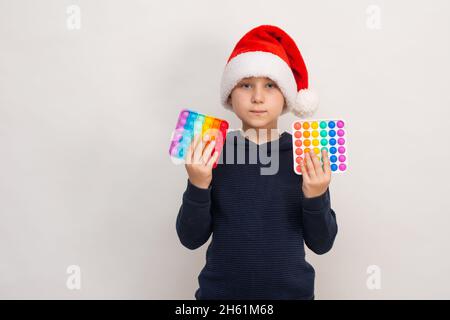 Ein Junge in Santa Helferhut hält einen Pop it in seinen Händen. Mock up Stockfoto