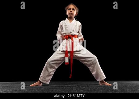 Ein kleines Mädchen, junges Karate in Kampfhaltung isoliert über dunklem Hintergrund. Konzept von Sport, Bildung, Fähigkeiten Stockfoto