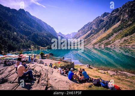 Wanderer machen eine Pause am Ufer des Sees Gaube, Cauterets, in den französischen Pyrenäen. Es ist von den Gipfeln Mayouret, Paloumeres und Gaube umgeben. Stockfoto