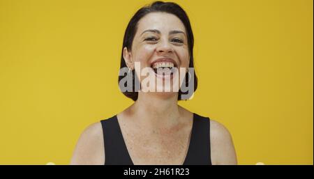 Attraktive Frau mittleren Alters mit einem schönen Lächeln auf der gelben Wand. Ziemlich ältere Frau, erfolgreiches Vertrauen. Stockfoto