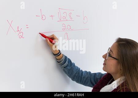 Brillanten Schüler, der mathematische Gleichung löst. Blonde junge Mädchen schreiben mit rotem Stift auf weißem Brett. Intelligente Frau Konzept, Lehrer erklären Problem Stockfoto