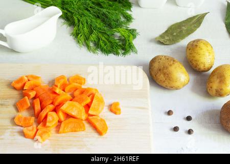 Zutaten für die Zubereitung von Fischsuppe. Die Karotten werden auf einem Holzschneidebrett mit einem Gemüsemesser in halbe Scheiben geschnitten. Lohikeitto ist ein traditionelles Stockfoto