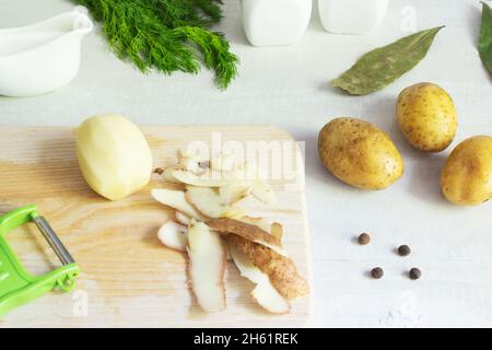 Zutaten für die Zubereitung von Fischsuppe. Die Kartoffeln werden geschält und mit einem Gemüsemesser auf einem Holzschneidebrett gewürfelt. Lohikeitto ist ein traditionelles F Stockfoto