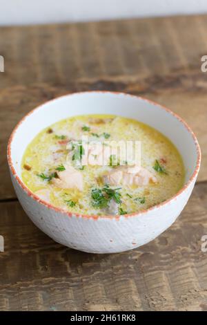 Lachs- und Cremefischsuppe in einer weißen Schüssel auf einem Holztisch. Lohikeitto ist eine traditionelle finnische und karelische Suppe. Rustikaler Stil. Horisontale Orientat Stockfoto