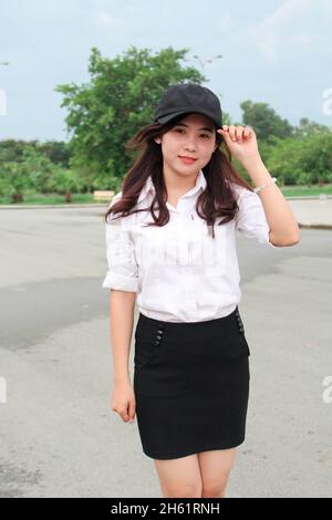 Schöne vietnamesische junge Frau in weißem Hemd und Rock mit schwarzer Mütze Stockfoto