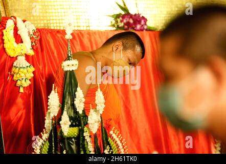 Bangkok, Thailand. November 2021. Ein buddhistischer Mönch, der eine Gesichtsmaske trägt, steht während des Tempels neben einem roten Tuch und wickelte rote Tücher um den goldenen Berg. Eifrige Anhänger versammelten sich, um den Chedi des Goldenen Berges mit einem heiligen roten Tuch zu umwickeln, was den Beginn des Wat Saket-Festivals markierte. Bevor sich die Gläubigen zu einer multikulturellen Parade anstellten, die aus Löwentänzern, traditionellen thailändischen Tänzern, Studenten der Tempelschule und spirituellen Brahmanen bestand. Namen von Familien und Angehörigen wurden auf die mehr als hundert Meter lange Stoffstrecke geschrieben, in der Hoffnung, Glück und Glück zu sichern Stockfoto