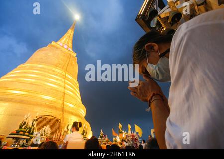 Bangkok, Thailand. November 2021. Eine Frau, die eine Gesichtsmaske trägt, betet während des Tempels vor einem Goldenen Berg und umwickelt den goldenen Berg mit rotem Tuch. Eifrige Anhänger versammelten sich, um den Chedi des Goldenen Berges mit einem heiligen roten Tuch zu umwickeln, was den Beginn des Wat Saket-Festivals markierte. Bevor sich die Gläubigen zu einer multikulturellen Parade anstellten, die aus Löwentänzern, traditionellen thailändischen Tänzern, Studenten der Tempelschule und spirituellen Brahmanen bestand. Namen von Familien und Angehörigen wurden in der Hoffnung, Glück und Glück zu sichern, auf die über hundert Meter lange Strecke des Gewebes geschrieben Stockfoto