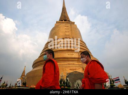 Bangkok, Thailand. November 2021. Buddhistische Mönche trugen Gesichtsmasken, die während des Tempels gesehen wurden, und wickelten rote Tücher um den goldenen Berg. Eifrige Anhänger versammelten sich, um den Chedi des Goldenen Berges mit einem heiligen roten Tuch zu umwickeln, was den Beginn des Wat Saket-Festivals markierte. Bevor sich die Gläubigen zu einer multikulturellen Parade anstellten, die aus Löwentänzern, traditionellen thailändischen Tänzern, Studenten der Tempelschule und spirituellen Brahmanen bestand. Namen von Familien und Angehörigen wurden in der Hoffnung, Glück und Segen zu sichern, auf das über hundert Meter lange Gewebe geschrieben. Quelle: SOPA Images Stockfoto