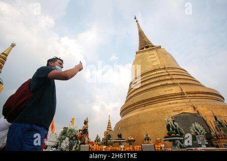 Bangkok, Thailand. November 2021. Ein Tourist macht während des Tempels Fotos vom Goldenen Berg und umwickelt den goldenen Berg mit rotem Tuch. Eifrige Anhänger versammelten sich, um den Chedi des Goldenen Berges mit einem heiligen roten Tuch zu umwickeln, was den Beginn des Wat Saket-Festivals markierte. Bevor sich die Gläubigen zu einer multikulturellen Parade anstellten, die aus Löwentänzern, traditionellen thailändischen Tänzern, Studenten der Tempelschule und spirituellen Brahmanen bestand. Namen von Familien und Angehörigen wurden in der Hoffnung, Glück und Segen zu sichern, auf das über hundert Meter lange Gewebe geschrieben. Kredit: SOPA Stockfoto