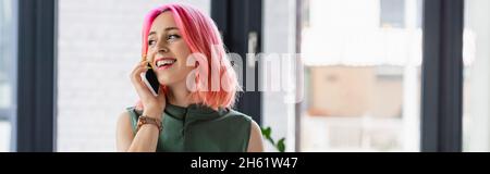 Fröhliche Geschäftsfrau mit rosa Haaren und piercing im Büro auf dem Smartphone sprechen, Banner Stockfoto