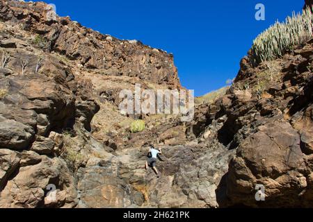 Tapferer Mann, der an sonnigen Tagen auf Gran Canaria, Spanien, auf den felsigen Berg klettert. Abenteurer Wandern auf den Kanarischen Inseln Stockfoto