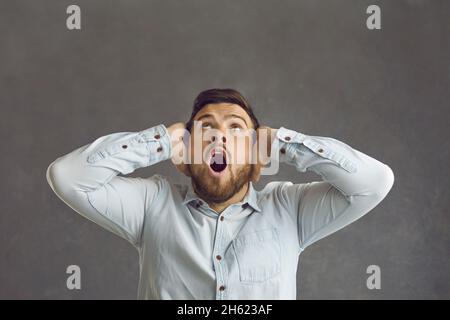 Studioporträt eines jungen Mannes, der etwas oben anschaut und vor Schock oder Angst keuchte Stockfoto