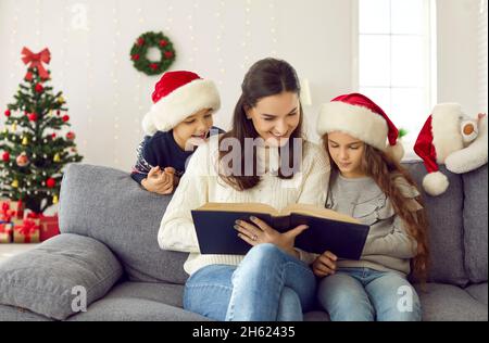 Glückliche Familie, die im dekorierten Wohnzimmer auf der Couch sitzt und ein Buch mit Weihnachtsgeschichten liest Stockfoto