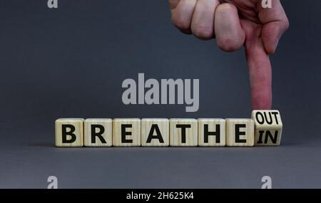 Symbol „Einatmen“ und „Ausatmen“. Doktor dreht einen Holzwürfel und ändert Worte atmen ein, um auszuatmen. Schöner grauer Hintergrund, Kopierbereich. Medizinisch, lif Stockfoto