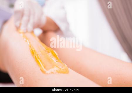 Zugeschnittenes Foto des Wachsepilierverfahrens zum Entfernen von Haaren mit Zuckerpaste im Schönheitssalon, Beauty- und Körperpflegekonzept des Wellnesscenters. Stockfoto