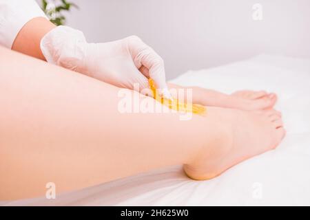 Professioneller Kosmetologe im Schönheitssalon, der Wachsen macht, ein Enthaarungsverfahren zum Entfernen von Haaren aus dem Bein mit Zuckerpaste auf Weiß Stockfoto
