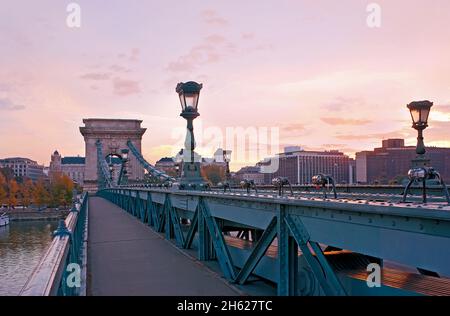 Die atemberaubende Kettenbrücke Szechenyi zur Goldenen Stunde mit Blick auf den Steinbogen, Metallkonstruktionen und die alten Straßenlaternen, Budapest, hing Stockfoto