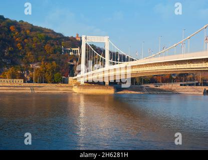 Die weiße Elisabethbrücke (Erzsebet HID) über die Donau gegen den Gellertberg mit Blick auf die St. Gellertstatue mit Kolonnade und buntem au Stockfoto