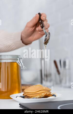 Beschnittene Ansicht einer Frau, die in der Küche Honig auf Pfannkuchen mit Beeren gießt Stockfoto