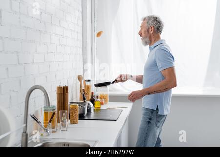 Seitenansicht eines reifen Mannes, der beim Kochen in der Küche Pfannkuchen warf Stockfoto