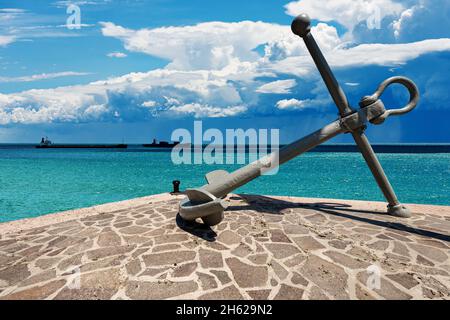 Großer Anker am Ufer des Meeres mit schöner Meereslandschaft im Hintergrund mit Schiffen und Cumulonimbuswolken am blauen Himmel. Mittelmeer. Stockfoto