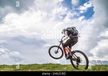 Wheelie mit E-Bike auf einem grünen Feld, ein Mann 37 Jahre alt, dolomiten, belluno, italien Stockfoto