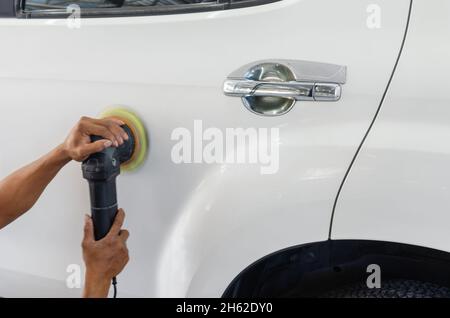 Mann bei der Arbeit Zum polieren, beschichten Autos. Polieren des Autos hilft Verunreinigungen auf der Oberfläche des Autos zu beseitigen. das Einwachsen der Auto Oberfläche c Stockfoto