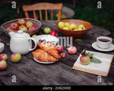 Schöner Herbst Stillleben in Apfelgarten, alten Tisch mit Tasse, Teekannen, Äpfel und Buch. Herbst-Kurzurlaub, Apfelernte und Erntedankfest con Stockfoto