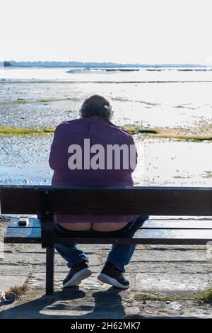 england, hampshire, hayling Island, lustige Rückansicht des übergewichtigen Mannes, der auf der Bank sitzt Stockfoto