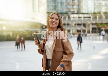 Shopping am Black Friday. Geschäftsfrau beim Gehen. Mobile App. Moderne Architektur. Winterkleidung. Weihnachten festlich. Technologie-Mitarbeiter. Stockfoto