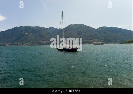 Ein Boot auf dem Wasser mit einigen Bergen im Hintergrund - lago di maggiore Stockfoto