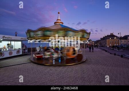 Strandpromenade in Saint-Aubin-sur-Mer zur blauen Stunde mit einem schönen Kinderkarussell in Bewegung und einem Süßigkeitengeschäft im Vordergrund. Stockfoto