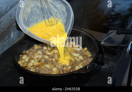 In einem Dtuchofen werden Eier auf Würstchen und Kartoffelrösti gegossen; im Freien wird ein Auflauf zum Frühstück zubereitet Stockfoto