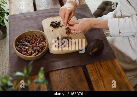 Hände schälen Bio-Kakaobohnen auf Holztisch, Kakaobohnen, handwerkliche Schokolade in rustikalem Stil für die Zeremonie auf dem Tisch. Degustation Stockfoto