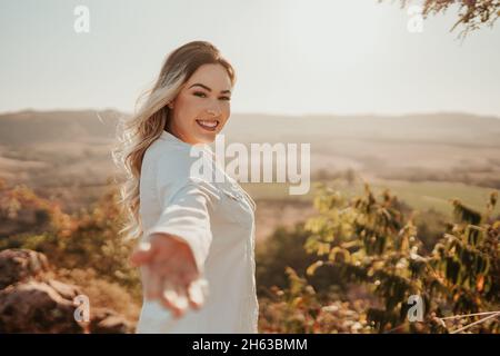 Eine lateinische Frau, die sich zur Kamera streut und zu einer Reise einlädt. Kommen Sie mit mir. Stockfoto