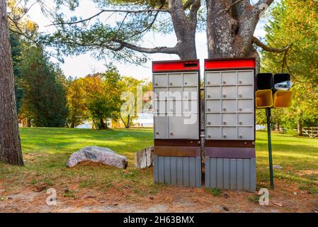 Alte Gemeindepostfächer entlang einer Straße an einem sonnigen Herbsttag ist Im Hintergrund Ein öffentlicher Park am Flussufer zu sehen. Stockfoto